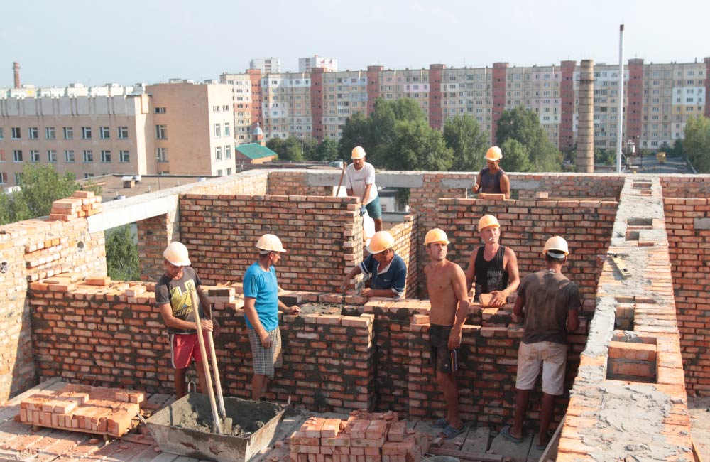 Бригада мулярів на будівництві на вул. Бідного, 5, завершує цегляну кладку чергового поверху будівлі