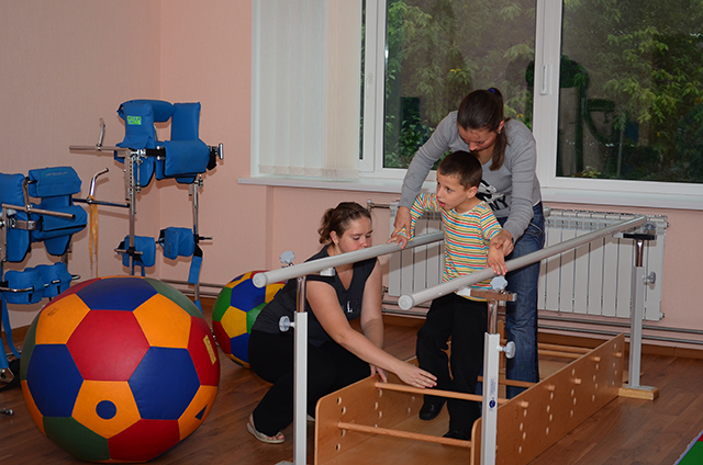 Физический реабилитолог Наталья Коркшина в тренажерном зале с маленьким пациентом и его мамой