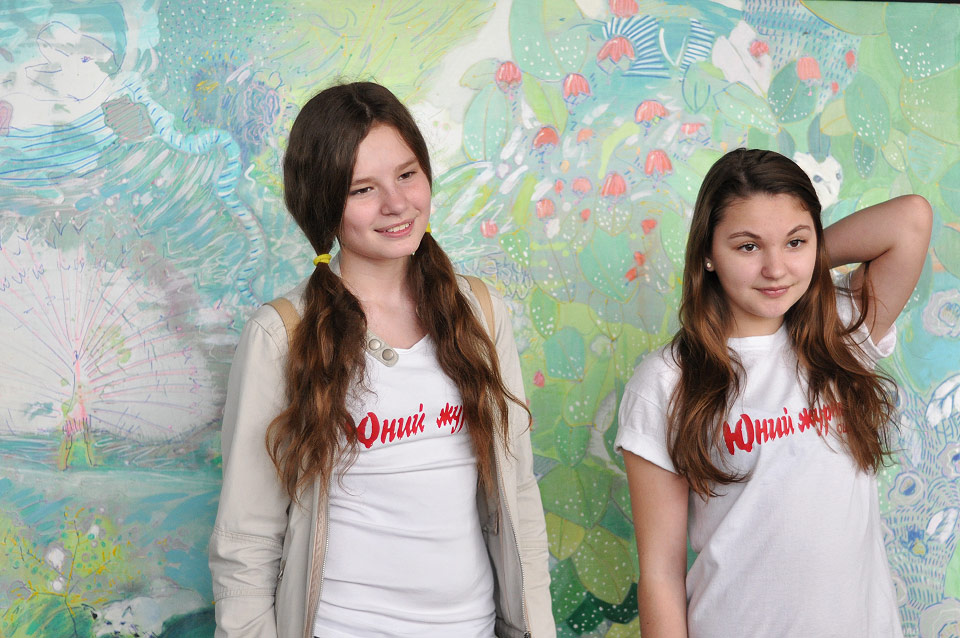Дві дівчинки із футболками «Юний журналіст» фотографуються на фоні третьої роботи Валерії Тарасенко.
